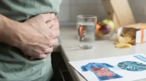Persona con le mani sull’addome accanto a un bicchiere d’acqua e un’illustrazione dell’apparato digerente