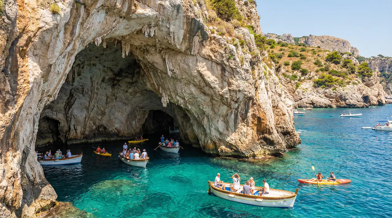 Ingresso di una grotta marina in una scogliera, con barche e kayak su acqua turchese lungo la costa italiana